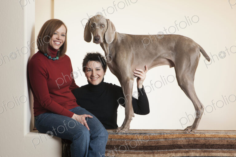 A same sex couple, two women posing with their Weimaraner pedigree dog.