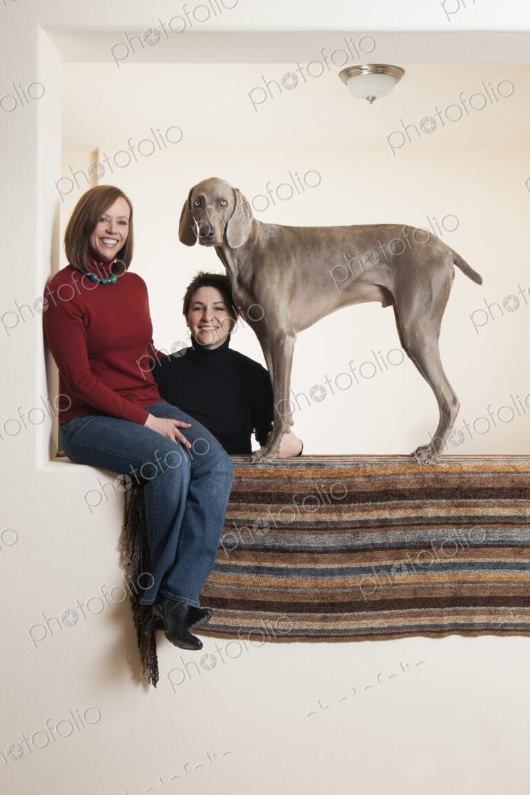 A same sex couple, two women posing with their Weimaraner pedigree dog.