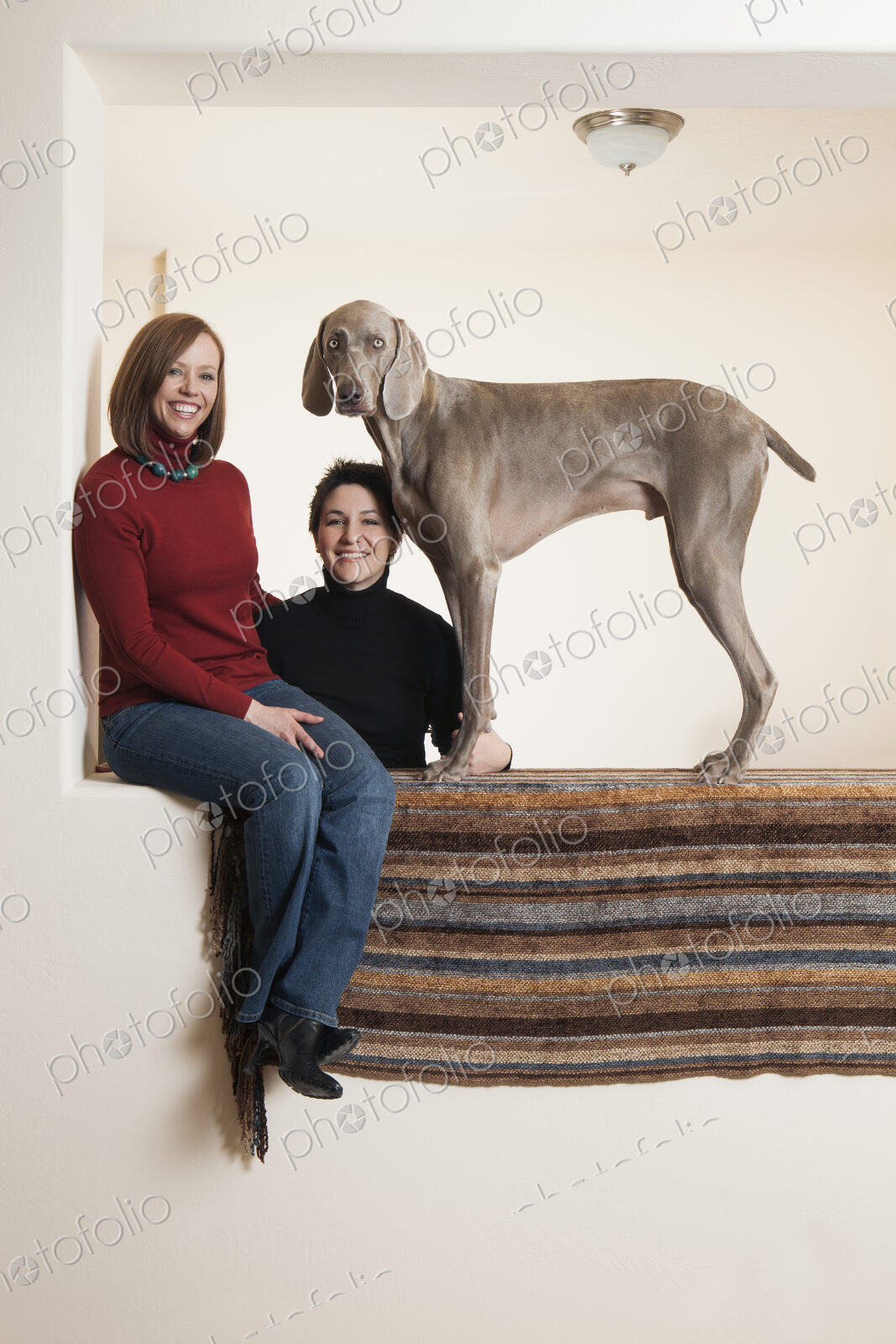 A same sex couple, two women posing with their Weimaraner pedigree dog.