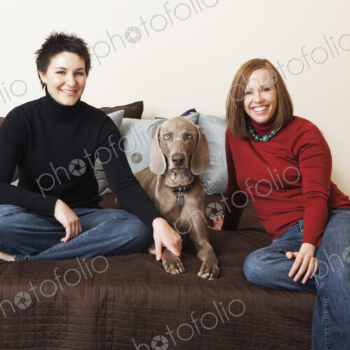 A same sex couple, two women posing with their weimeranar pedigree dog between them. A same sex couple, two women posing with their weimeranar pedigree dog between them.