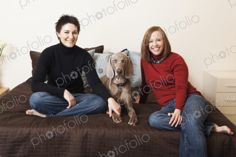 A same sex couple, two women posing with their weimeranar pedigree dog between them.