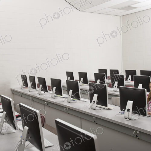 A school room, a computer lab with rows of screens and seating. A young person seated…