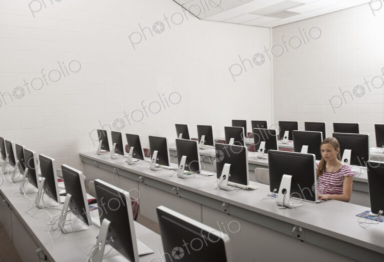 A school room, a computer lab with rows of screens and seating. A young person seated…