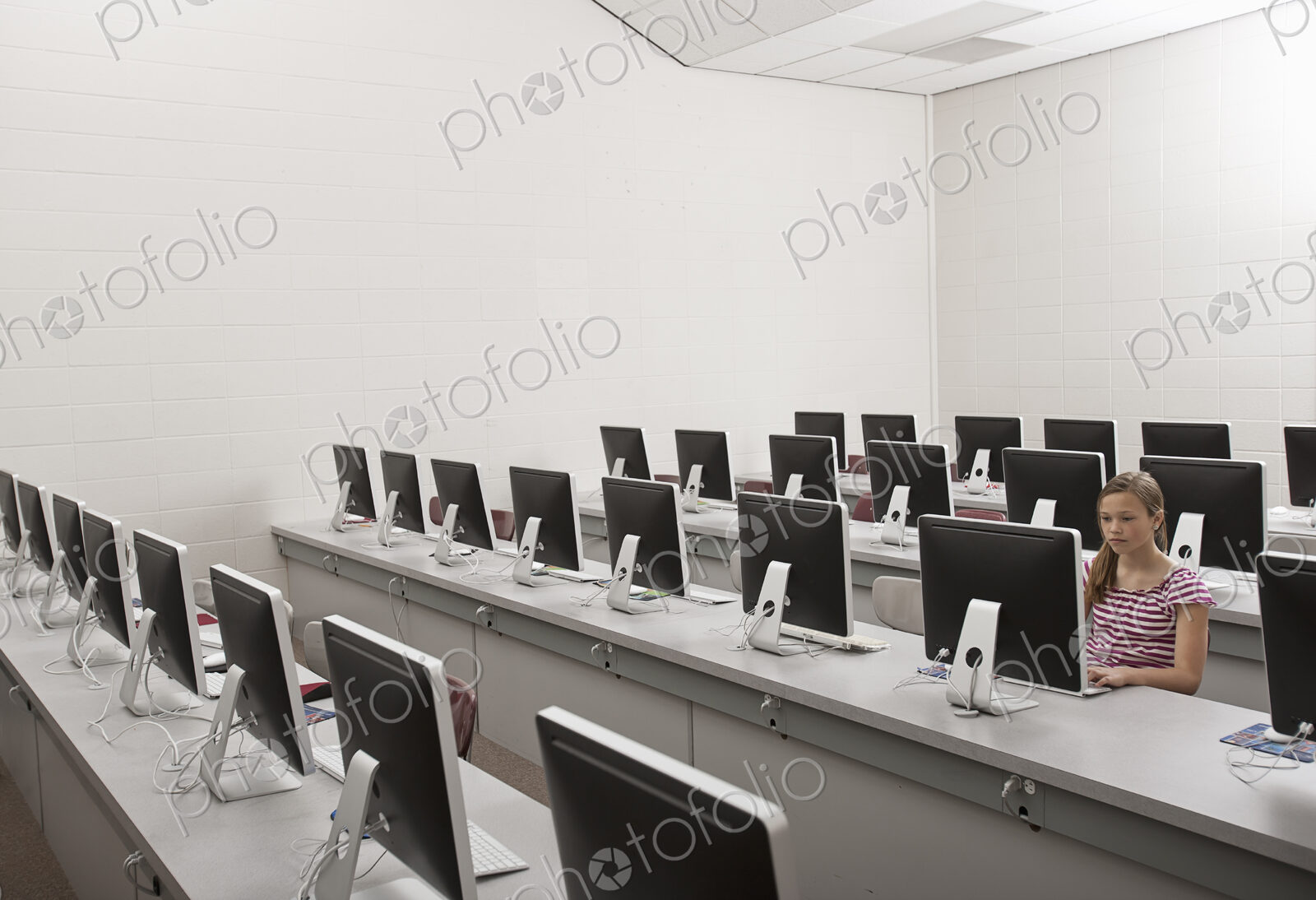 A school room, a computer lab with rows of screens and seating. A young person seated…
