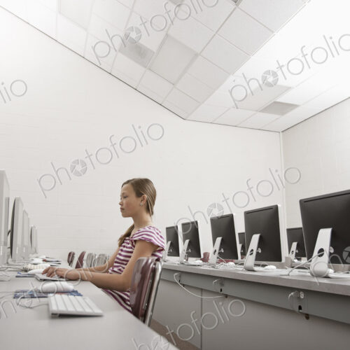 A school room, a computer lab with rows of screens and seating. A young person seated…