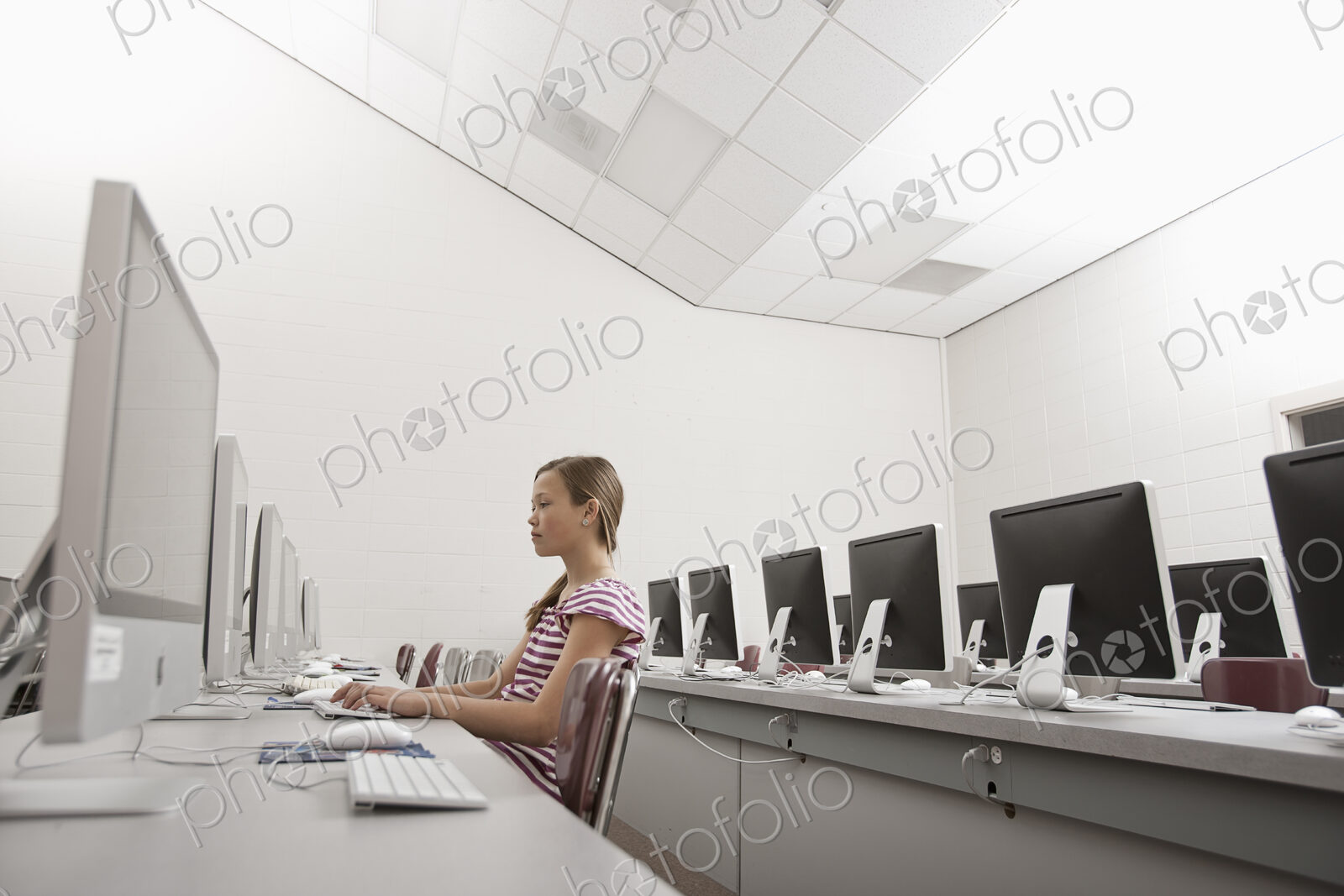 A school room, a computer lab with rows of screens and seating. A young person seated…