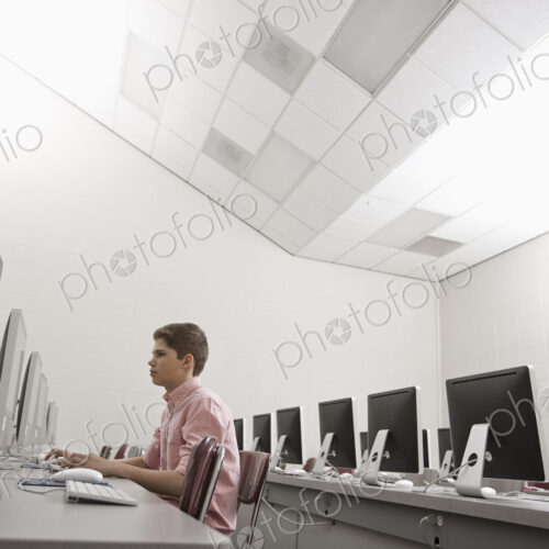 A school room, a computer lab with rows of screens and seating. A young person seated…