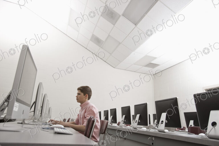 A school room, a computer lab with rows of screens and seating. A young person seated…