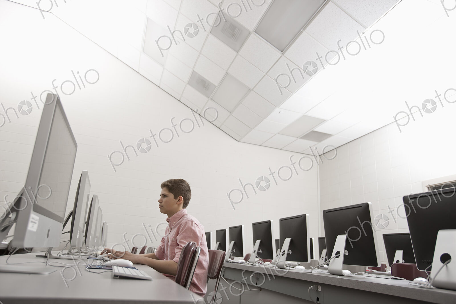 A school room, a computer lab with rows of screens and seating. A young person seated…