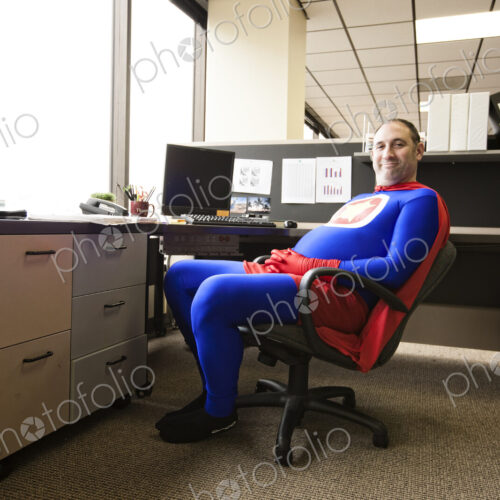 A self satisfied caucasian businessman super hero sits in his office cubicle. A self satisfied caucasian businessman super hero sits in his office cubicle.