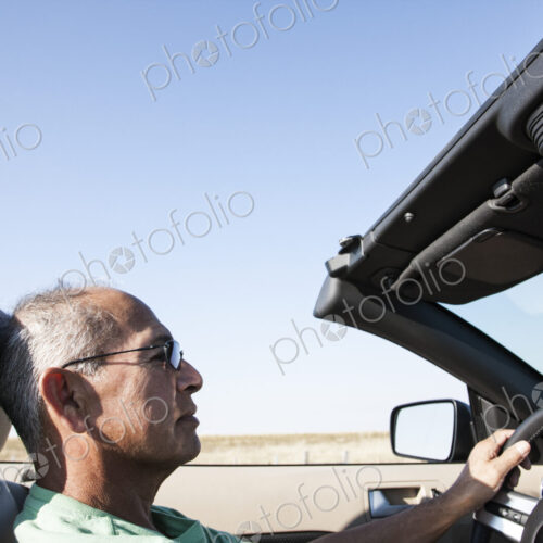 A senior Hispanic man at the wheel of his convertible sports car.