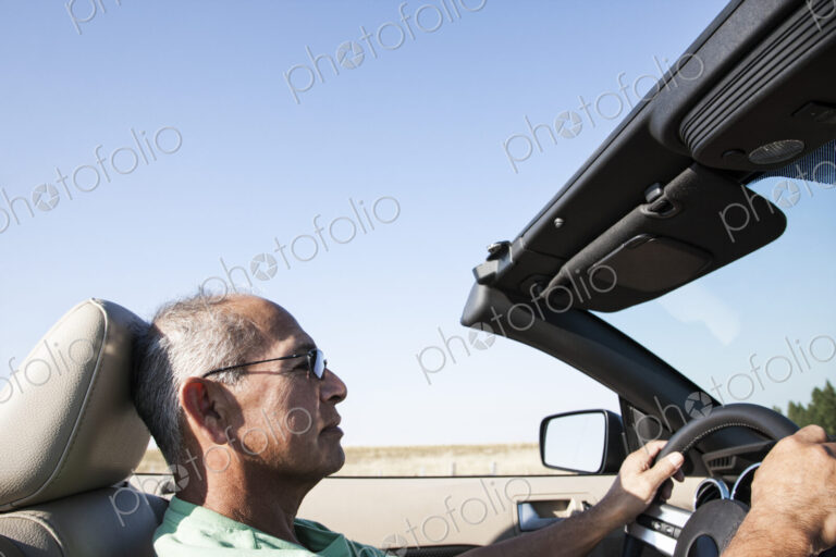 A senior Hispanic man at the wheel of his convertible sports car.