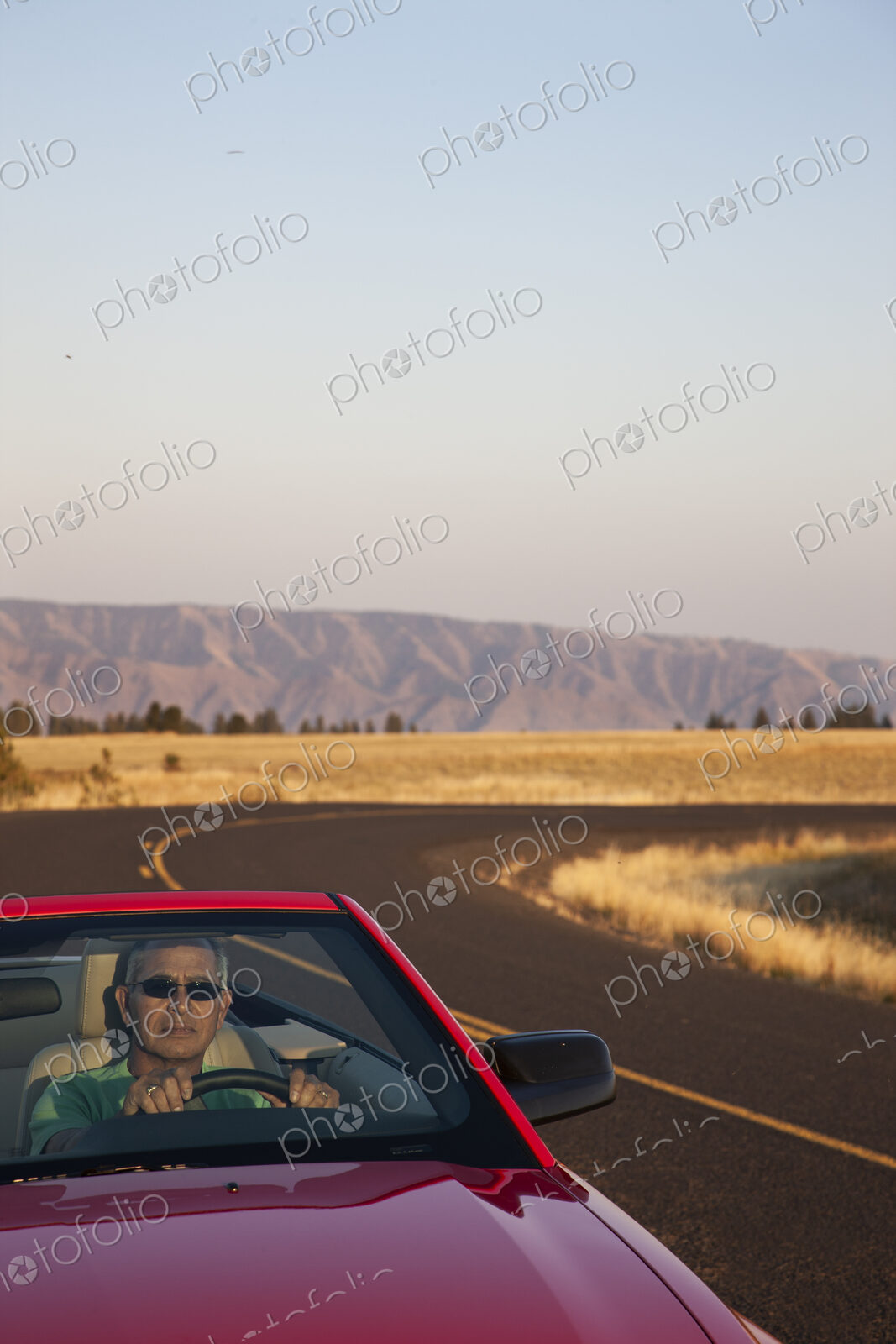 A senior Hispanic man at the wheel of his convertible sports car.