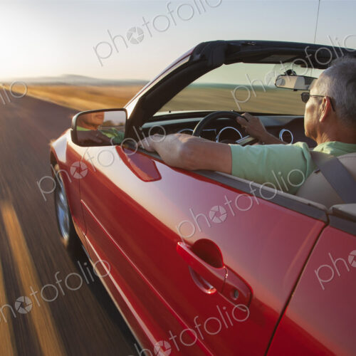 A senior Hispanic man at the wheel of his convertible sports car at sunset