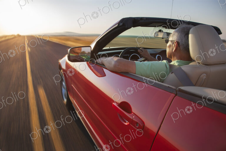 A senior Hispanic man at the wheel of his convertible sports car at sunset