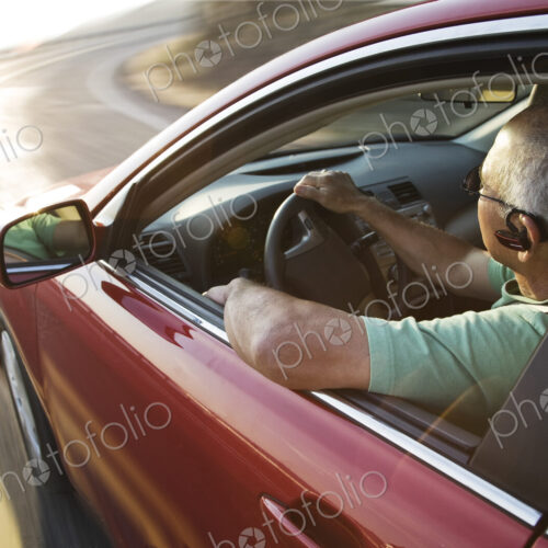 A senior Hispanic man at the wheel of his sedan with an ear piece for communications. A senior Hispanic man at the wheel of his sedan with an ear piece for communications.