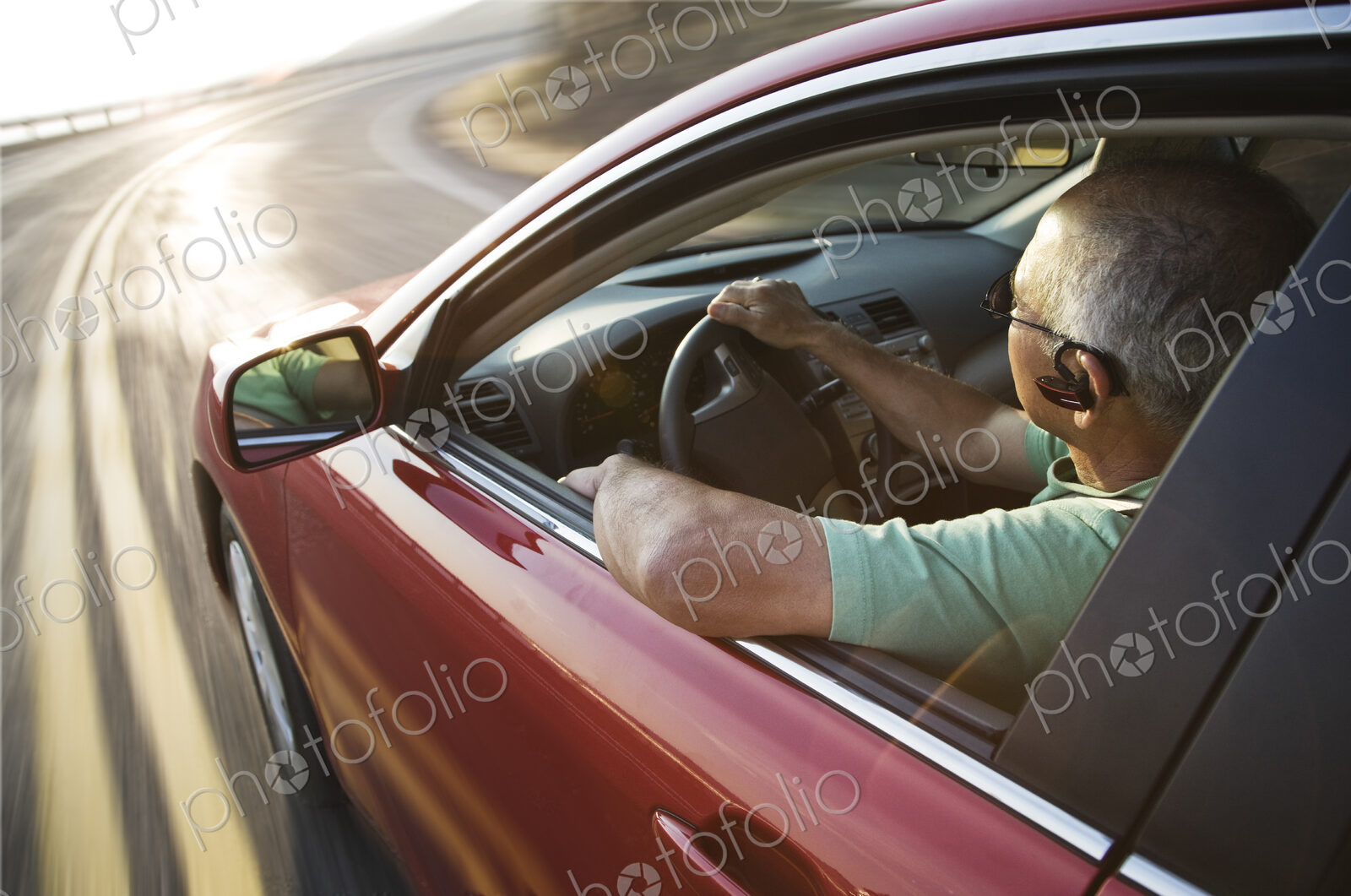 A senior Hispanic man at the wheel of his sedan with an ear piece for communications.