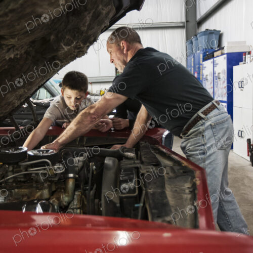 A senior caucasian male car mechanic showing his grandson how to work on a car engine.