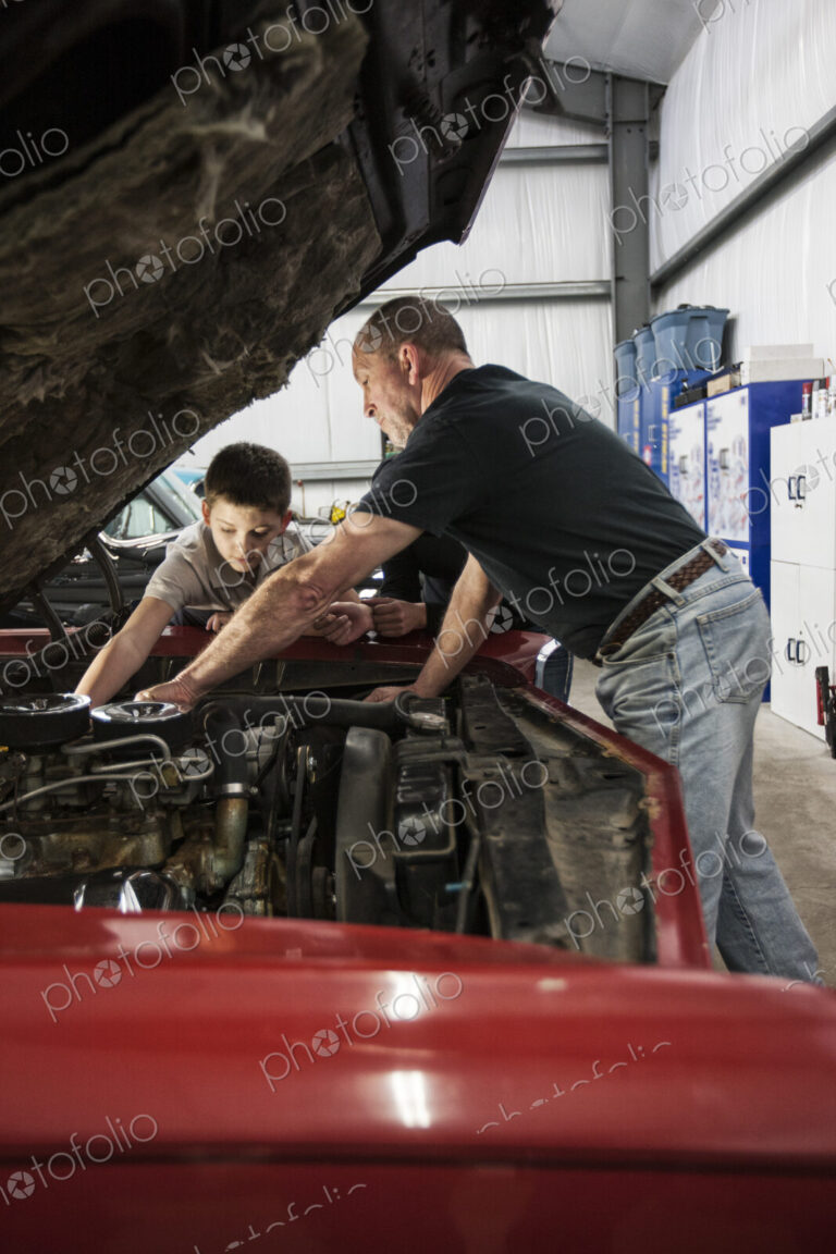 A senior caucasian male car mechanic showing his grandson how to work on a car engine.