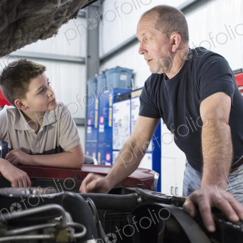 A senior caucasian male car mechanic showing his grandson how to work on a car engine.