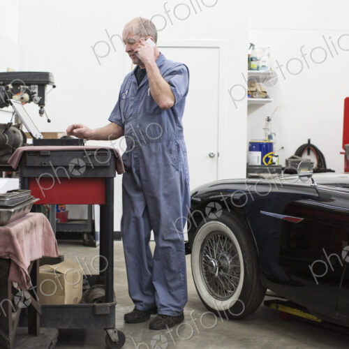 A senior caucasian male car mechanic working on his laptop computer in his classic car…