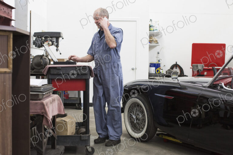A senior caucasian male car mechanic working on his laptop computer in his classic car…