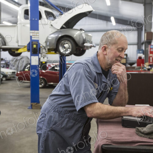 A senior caucasian male car mechanic working on his laptop computer in his classic car…