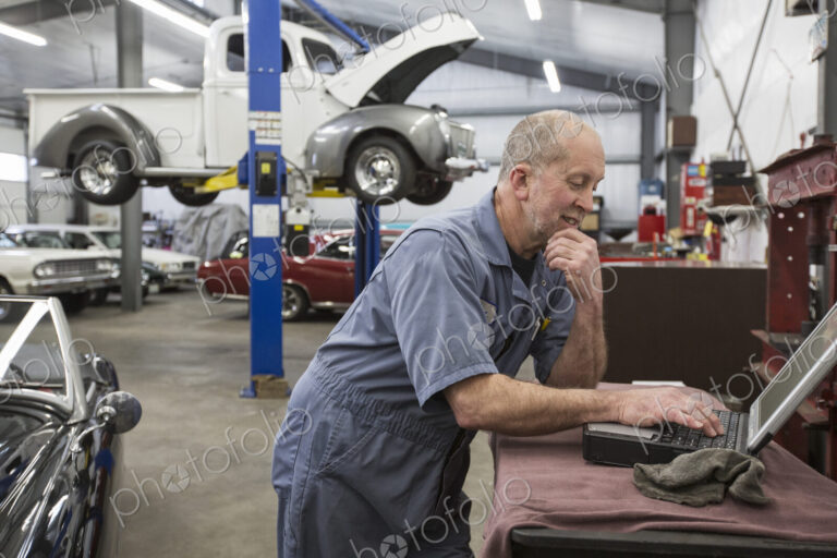A senior caucasian male car mechanic working on his laptop computer in his classic car…