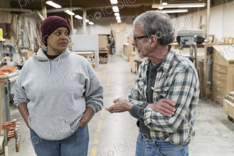 A senior causian male carpenter and a Black female carpenter discussion a project in a…