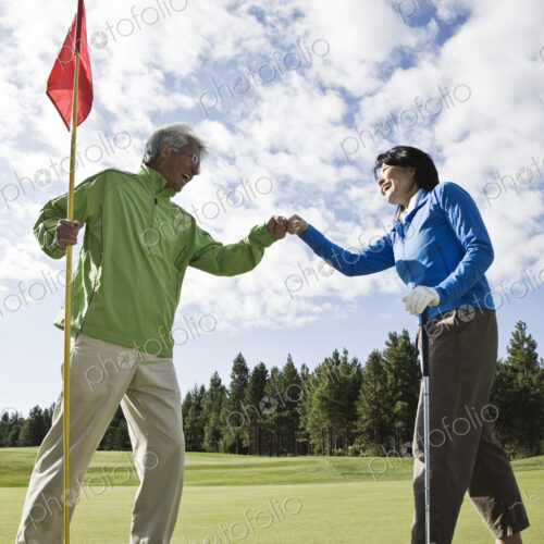 A senior couple doing a fist bump after making putt on a green.