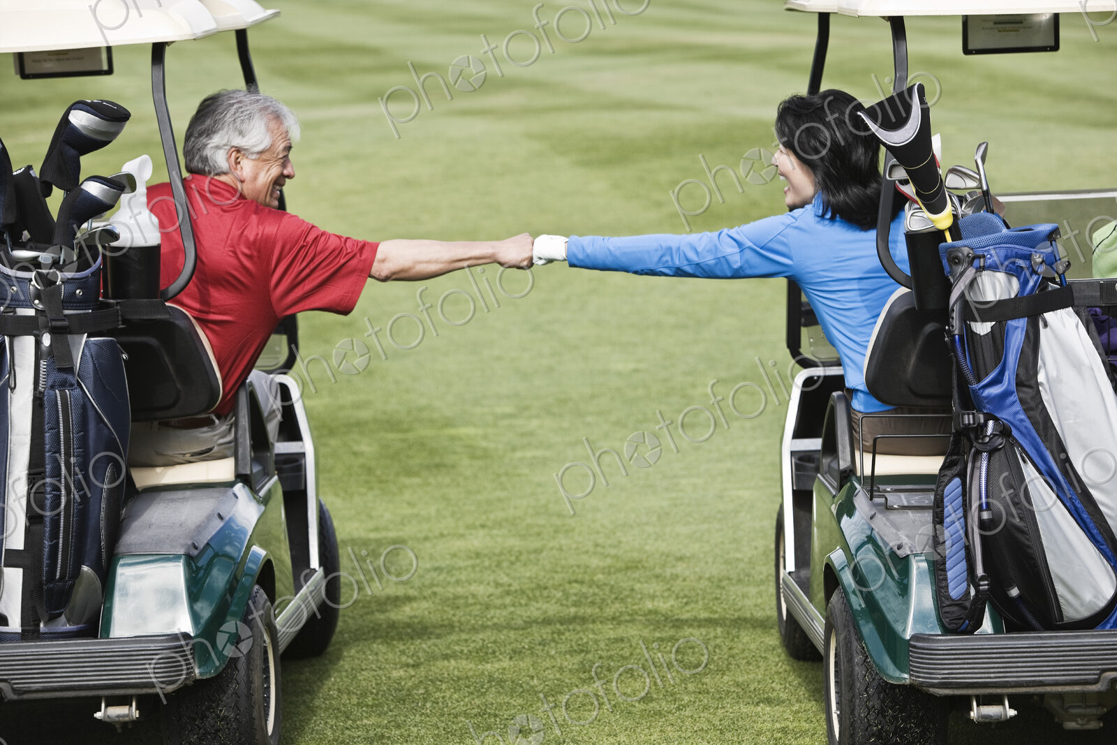 A senior couple doing a fist bump between golf carts on the fairway of a golf course.