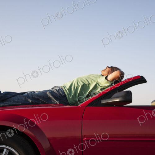 A senior male relaxing on the hood of his convertible sport car.