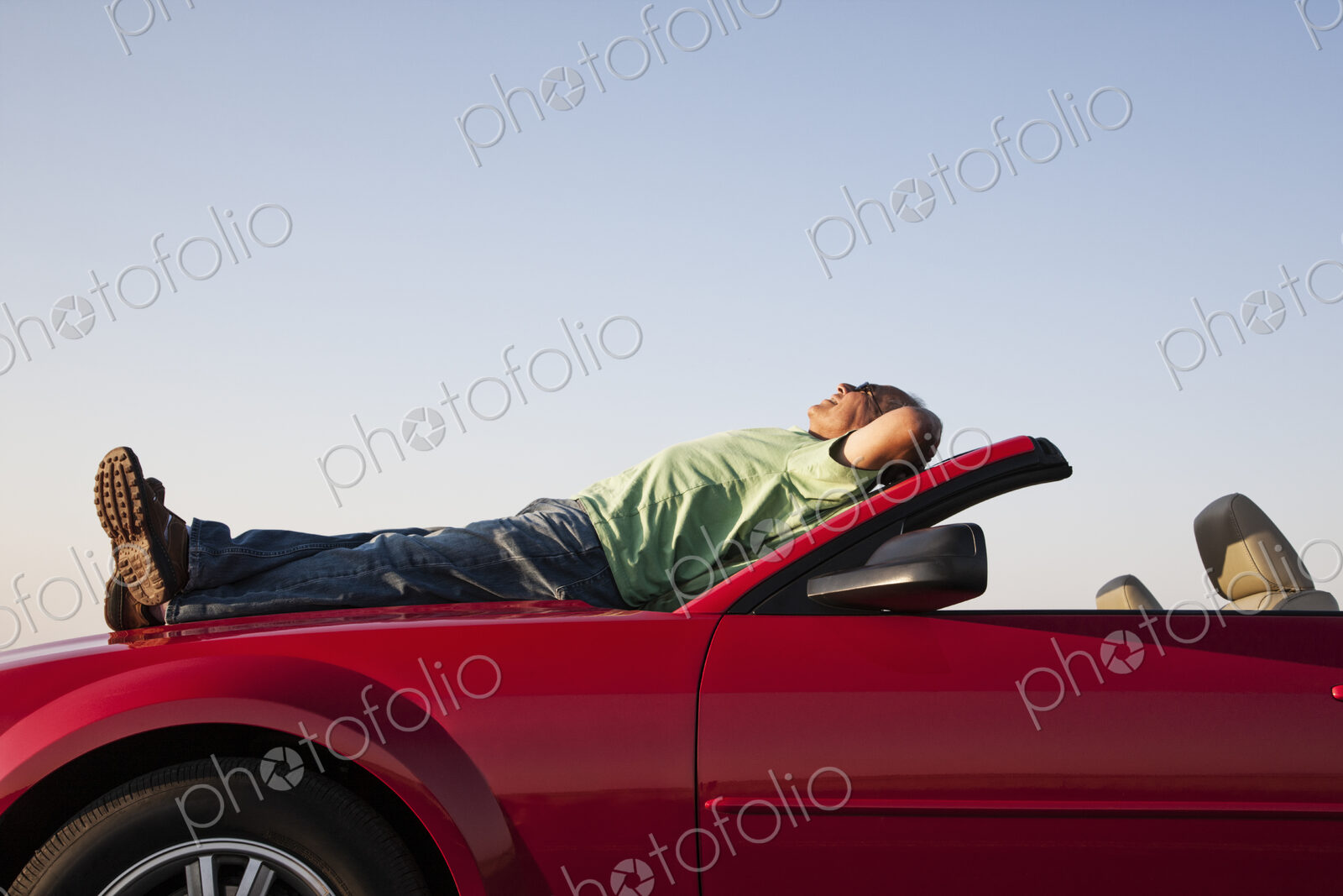 A senior male relaxing on the hood of his convertible sport car.