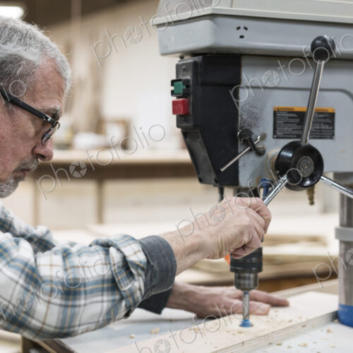 A senior man with glasses and beard in a woodworkers shop, using a machine. A senior man with glasses and beard in a woodworkers shop, using a machine.