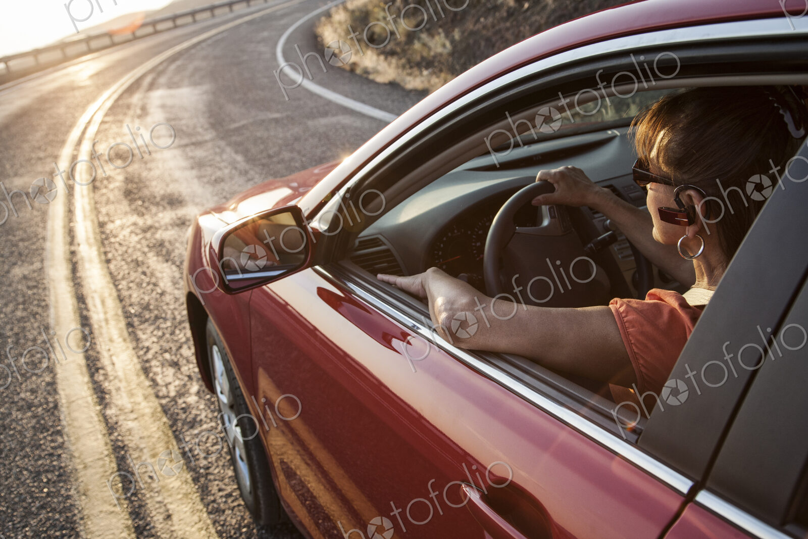 A senior woman at the wheel of her car with an ear piece for communications.