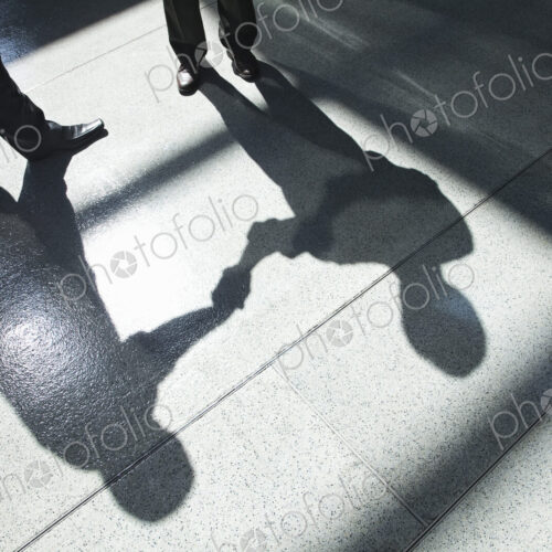 A shadow on a tiled floor of two businessmen shaking hands. A shadow on a tiled floor of two businessmen shaking hands.