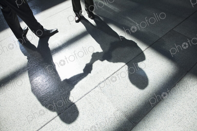 A shadow on a tiled floor of two businessmen shaking hands.