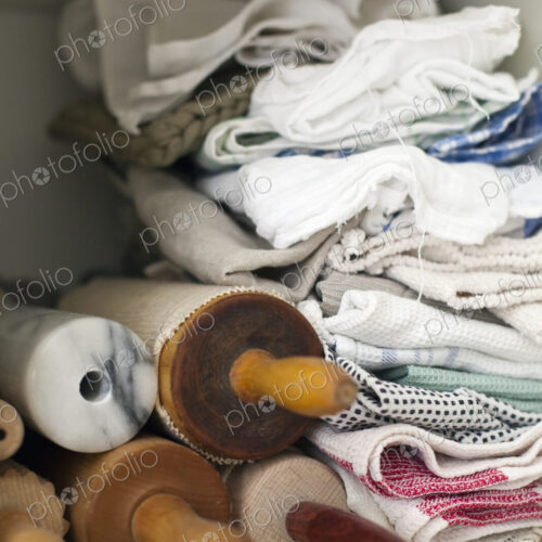 A shelf piled high with cloths, linen and a small stack of rolling pins or wooden…