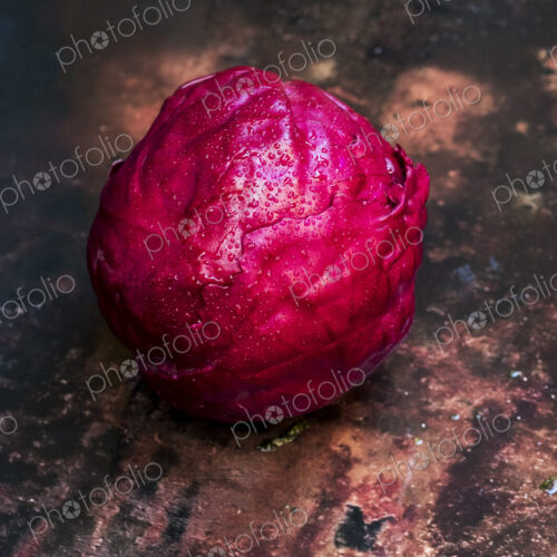 A shiny fresh red cabbage in its raw state, on a worn tabletop. A shiny fresh red cabbage in its raw state, on a worn tabletop.