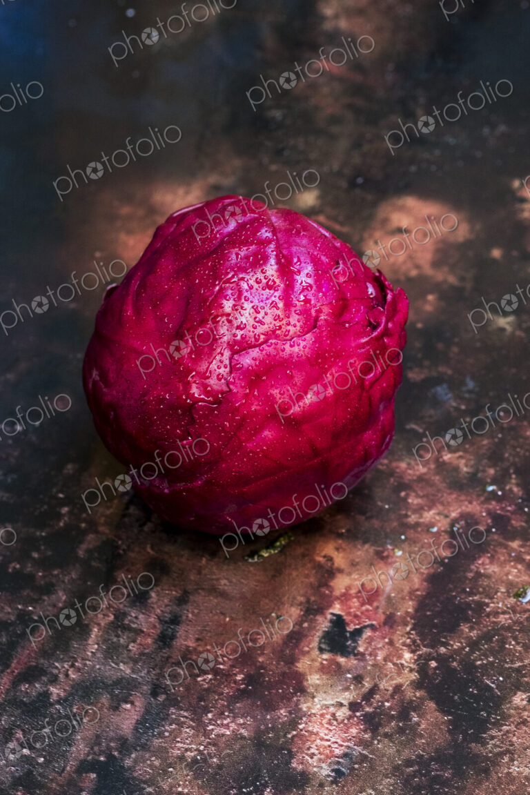 A shiny fresh red cabbage in its raw state, on a worn tabletop.