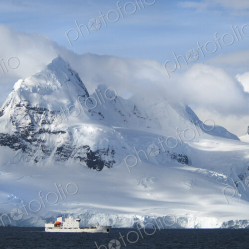 A ship under the towering shape of a mountain range. A ship under the towering shape of a mountain range.