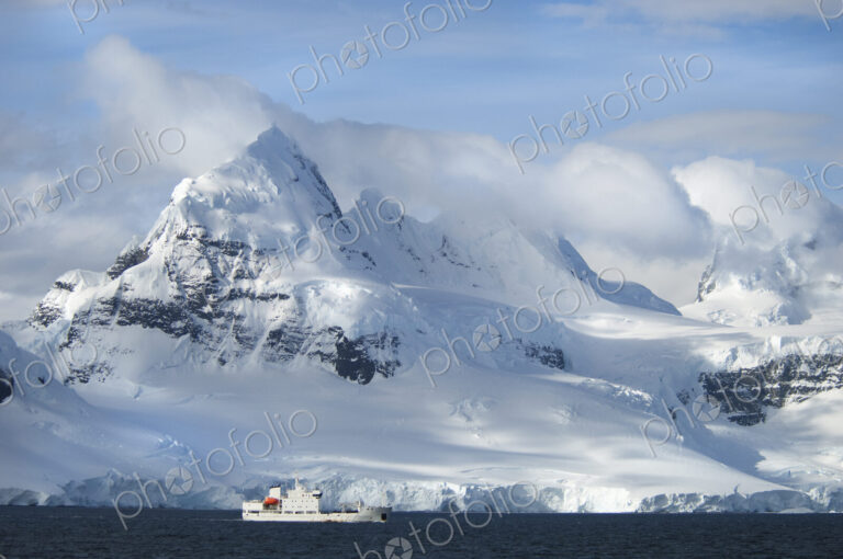 A ship under the towering shape of a mountain range.