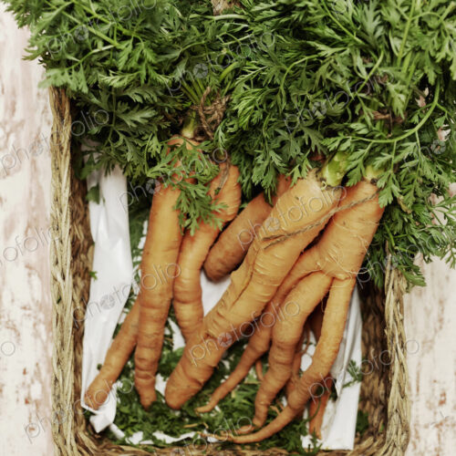 A shot of a bundle of carrots in a basket on a wooden surface, seen from above.