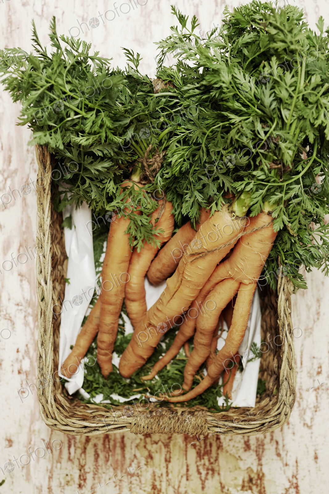 A shot of a bundle of carrots in a basket on a wooden surface, seen from above.