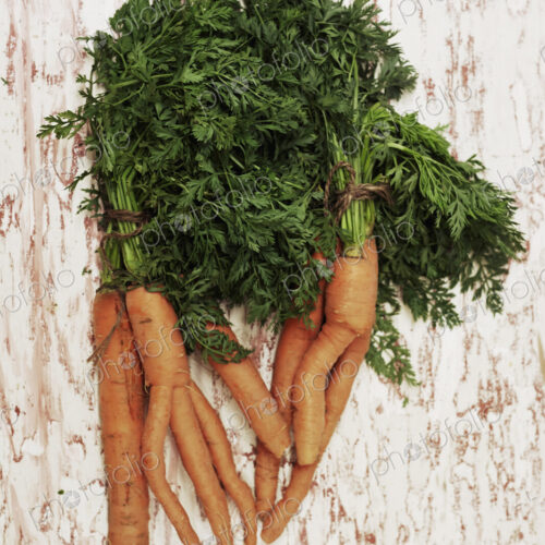 A shot of a bundle of carrots on a wooden surface, seen from above.
