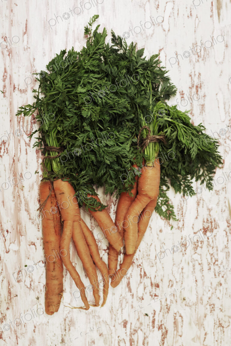 A shot of a bundle of carrots on a wooden surface, seen from above.