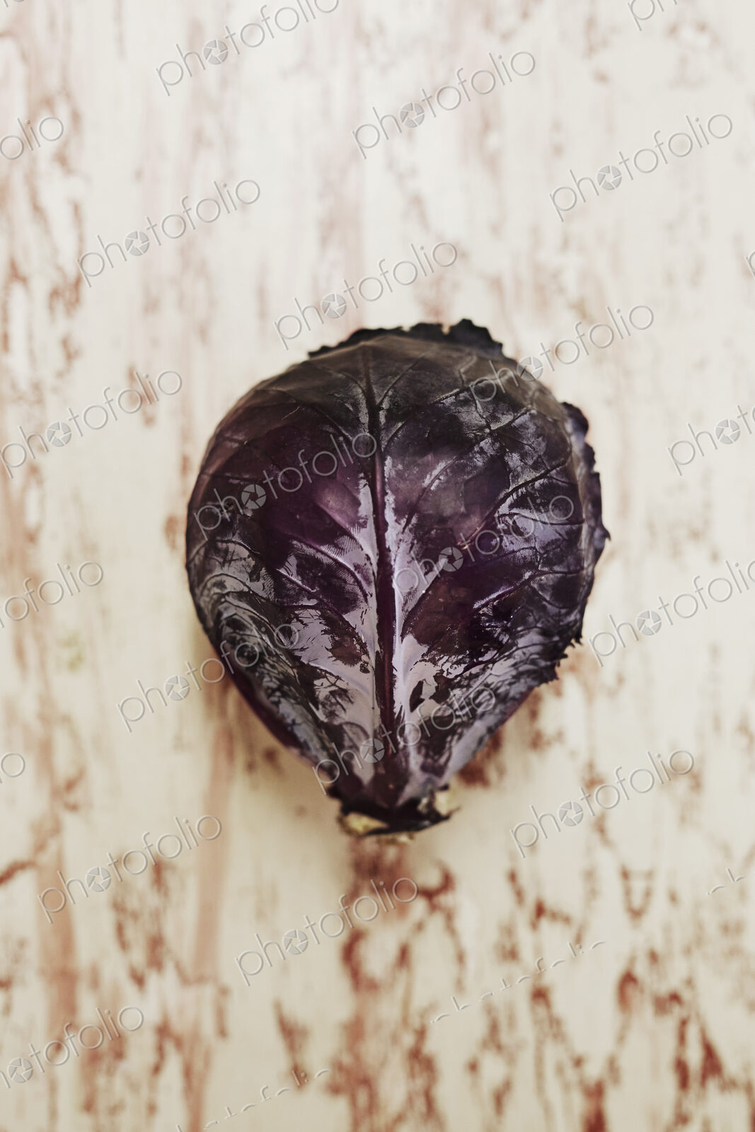A shot of a head of red cabbage on a wooden surface, seen from above.