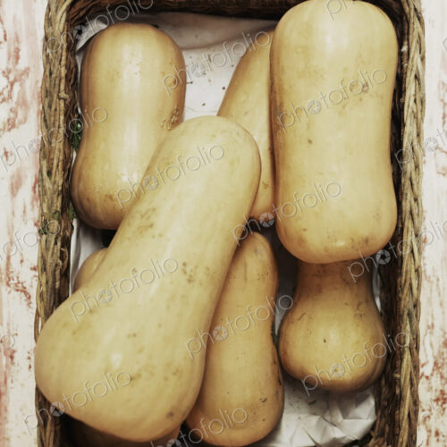 A shot of a pile of butternut squash in a basket on a wooden surface, seen from above.