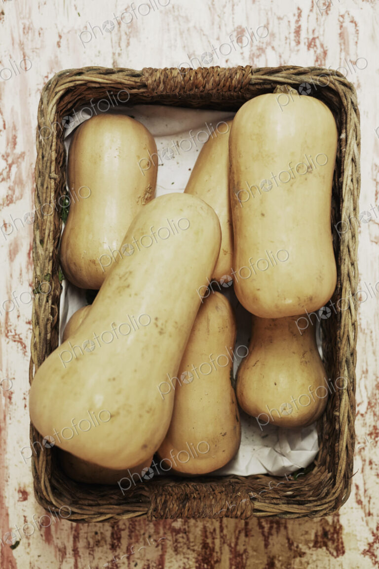 A shot of a pile of butternut squash in a basket on a wooden surface, seen from above.