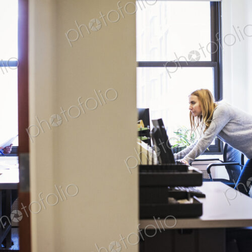 A shot of a young man sitting in an office looking at a cellphone, and a young woman…